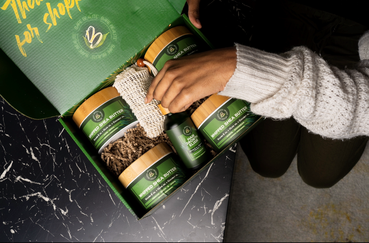 A person is holding a gift box containing various natural beauty products, including shea butter and soap.
