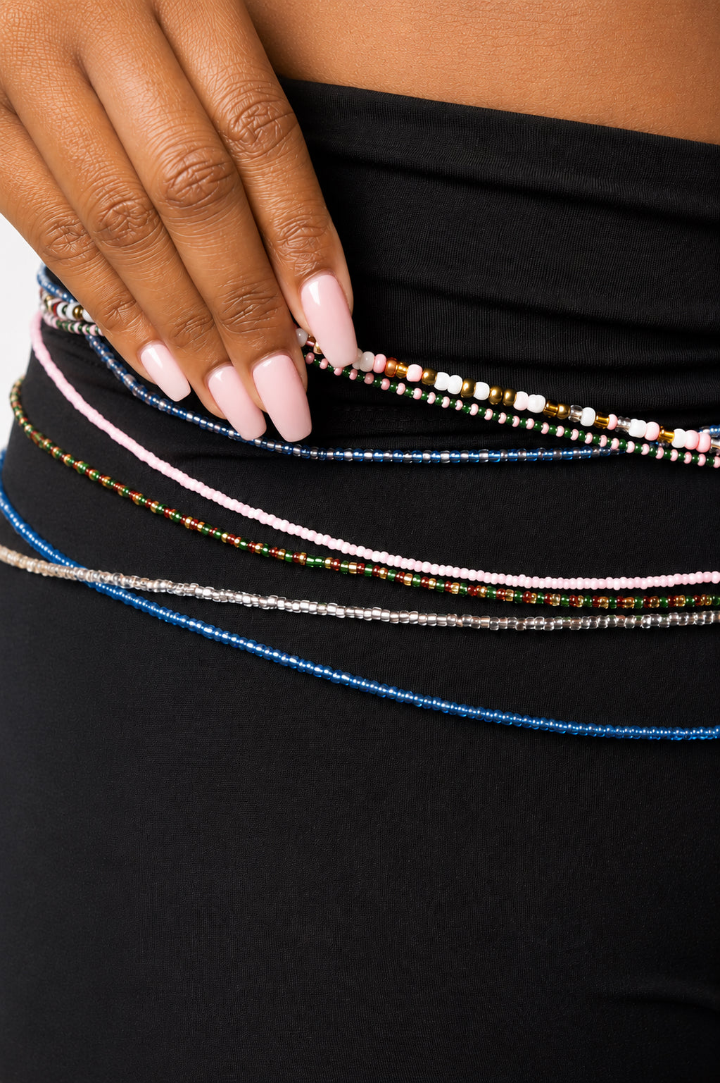 A close-up of a person wearing a black tights and accessorizing with multiple beaded waist chains in blue, pink, silver, and multicolor patterns.
