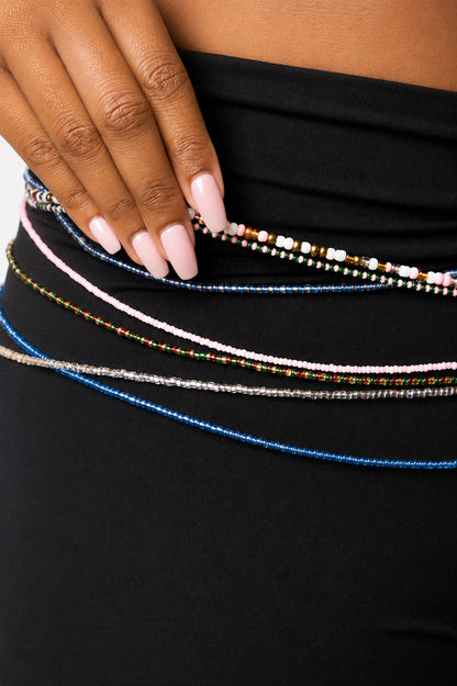 A close-up of a person wearing a black tights and accessorizing with multiple beaded waist chains in blue, pink, silver, and multicolor patterns.
