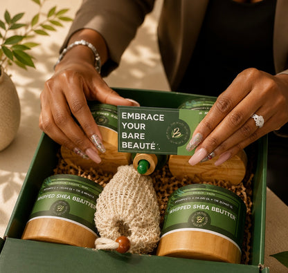 A gift box set of skincare products from Embrace Your Bare Beautie, featuring two jars of whipped shea butter, a small mesh bag, and a wooden stick, arranged in a green box with shredded paper. A person's hands are holding a card that says 'EMBRACE YOUR BARE BEAUTY'.