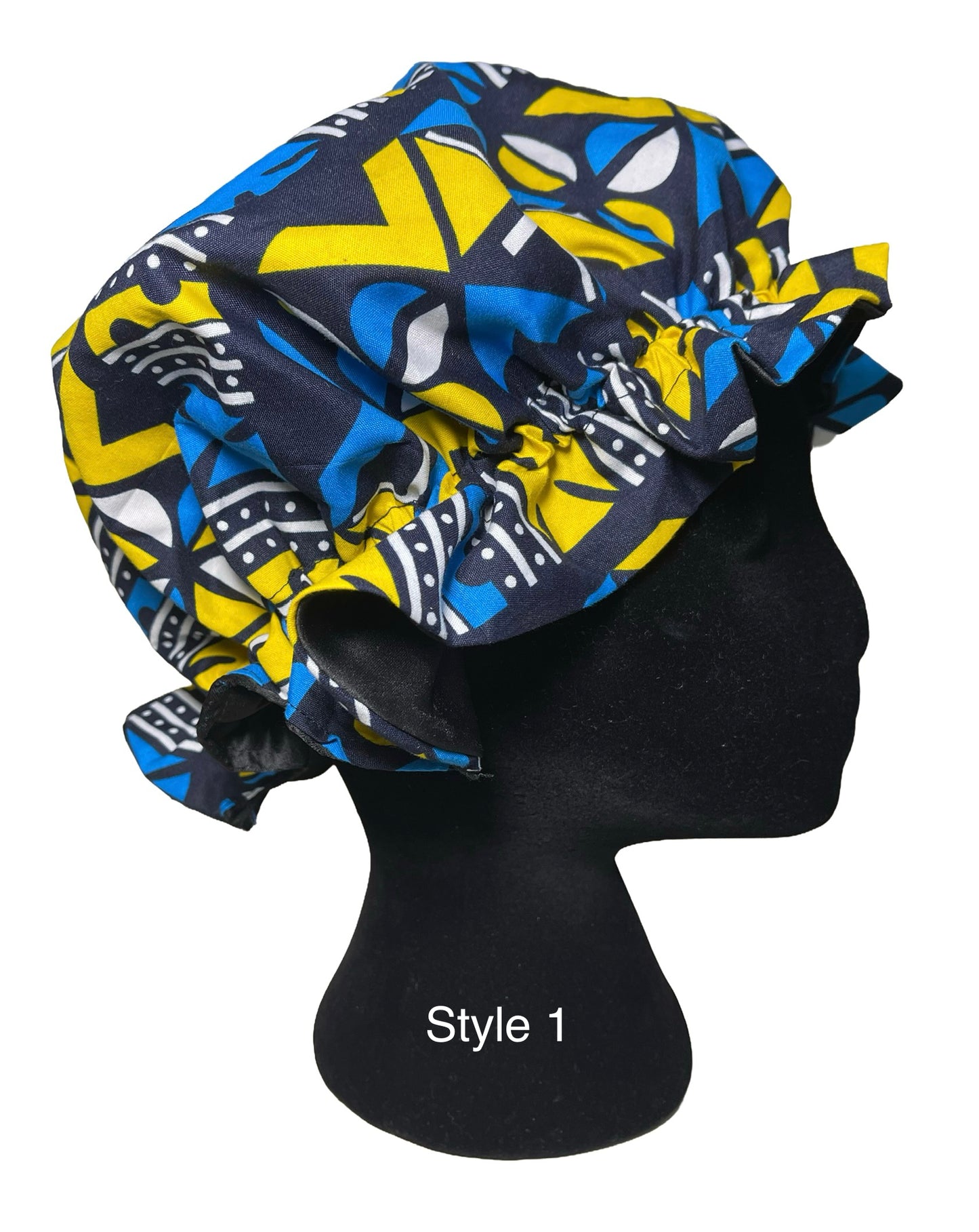 A bonnet with a bold geometric pattern in blue, yellow, and black, displayed on a black mannequin head against a white background.