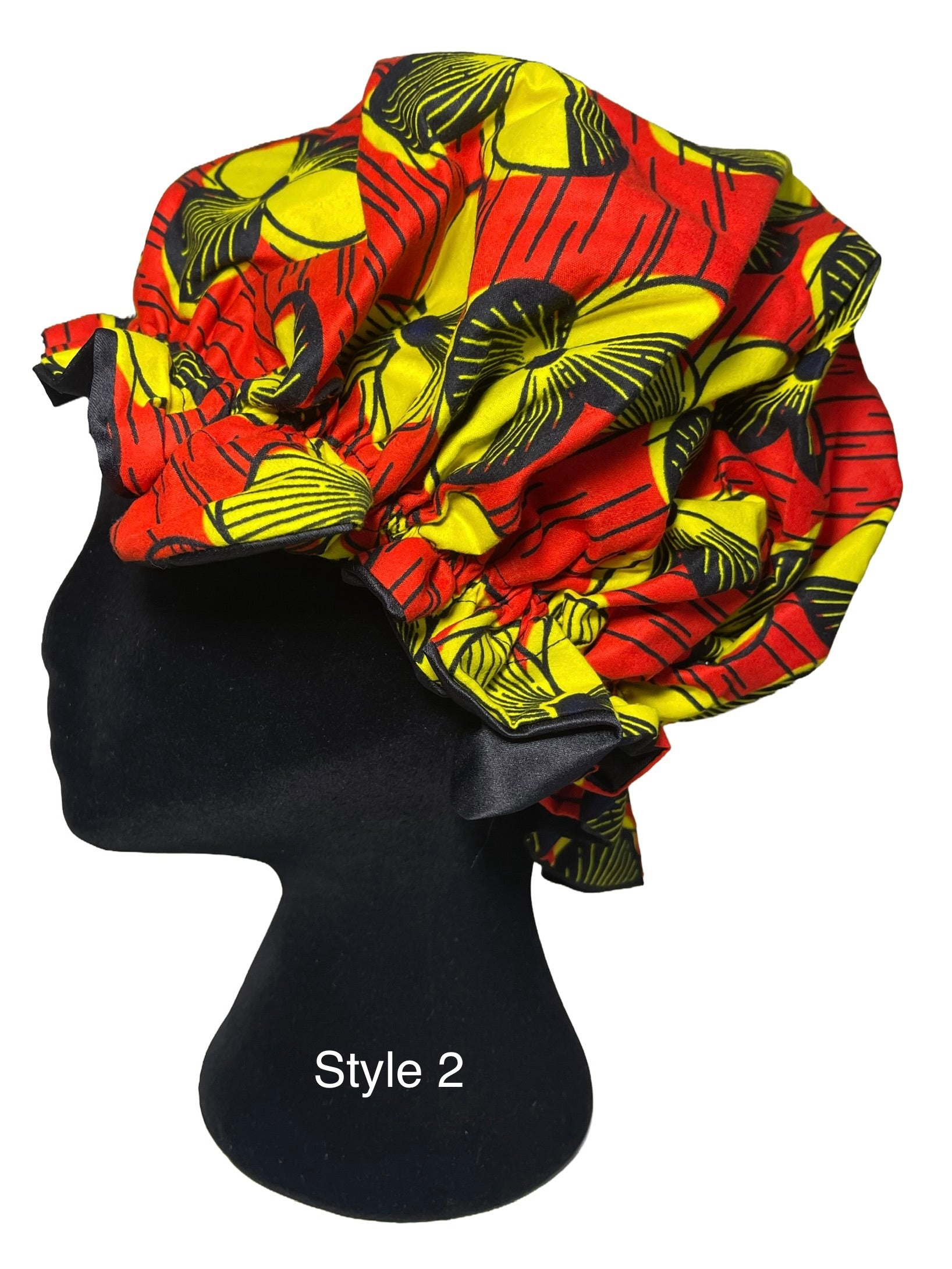 A large, voluminous bonnet with a bold red, yellow, and black floral pattern, styled on a black mannequin head. The text 'Style 2' is printed on the mannequin stand.