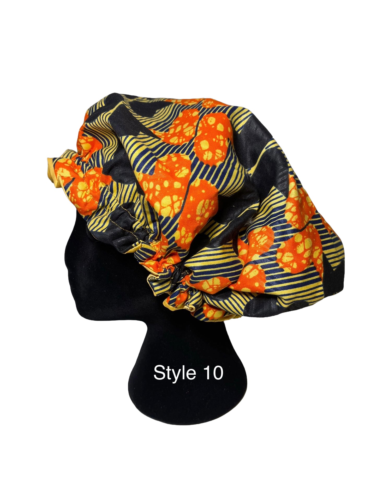 A black satin bonnet with a vibrant orange and yellow floral pattern and yellow-and-black striped accents, displayed on a black mannequin head against a white background.